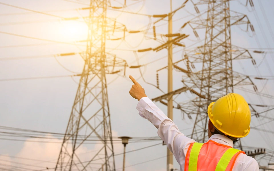 Eletricista trabalhando em um espaço aberto próximo a postes de alta tensão.